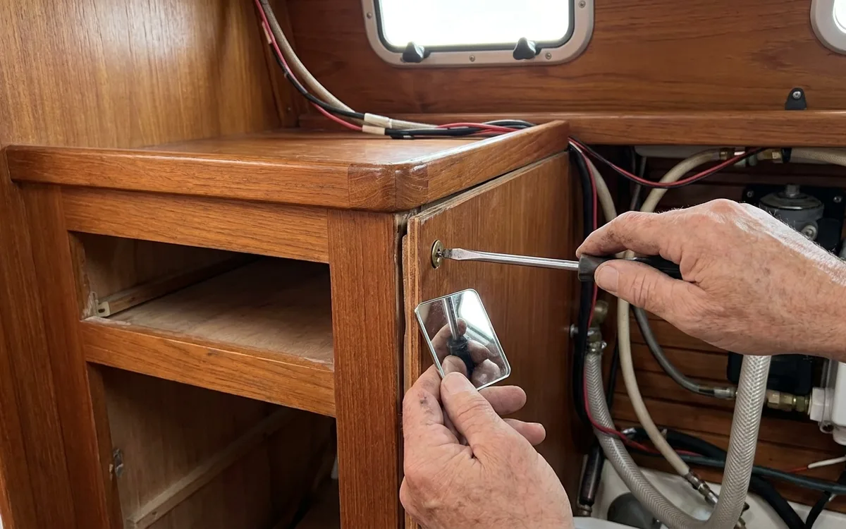 Hands loosen a cabinet screw while checking behind the joint for hoses and wiring.