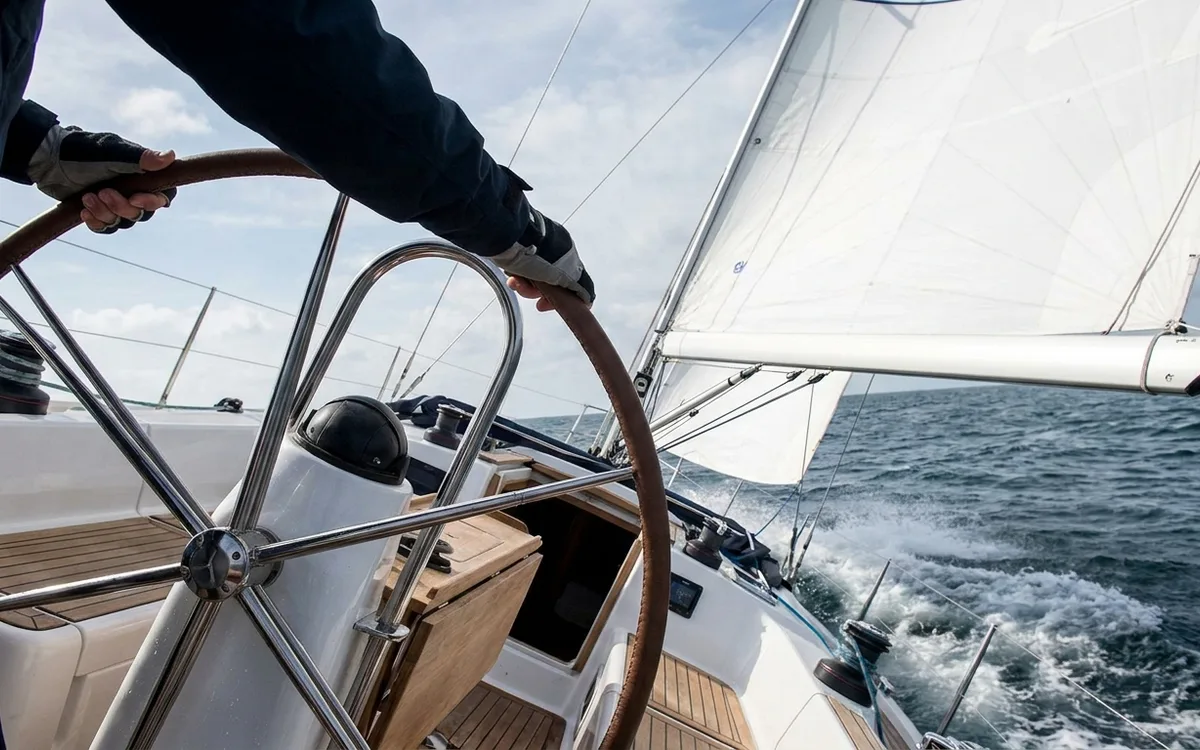 Hands make a small wheel correction while an X-Yachts boat sails close-hauled with a flat, trimmed mainsail.
