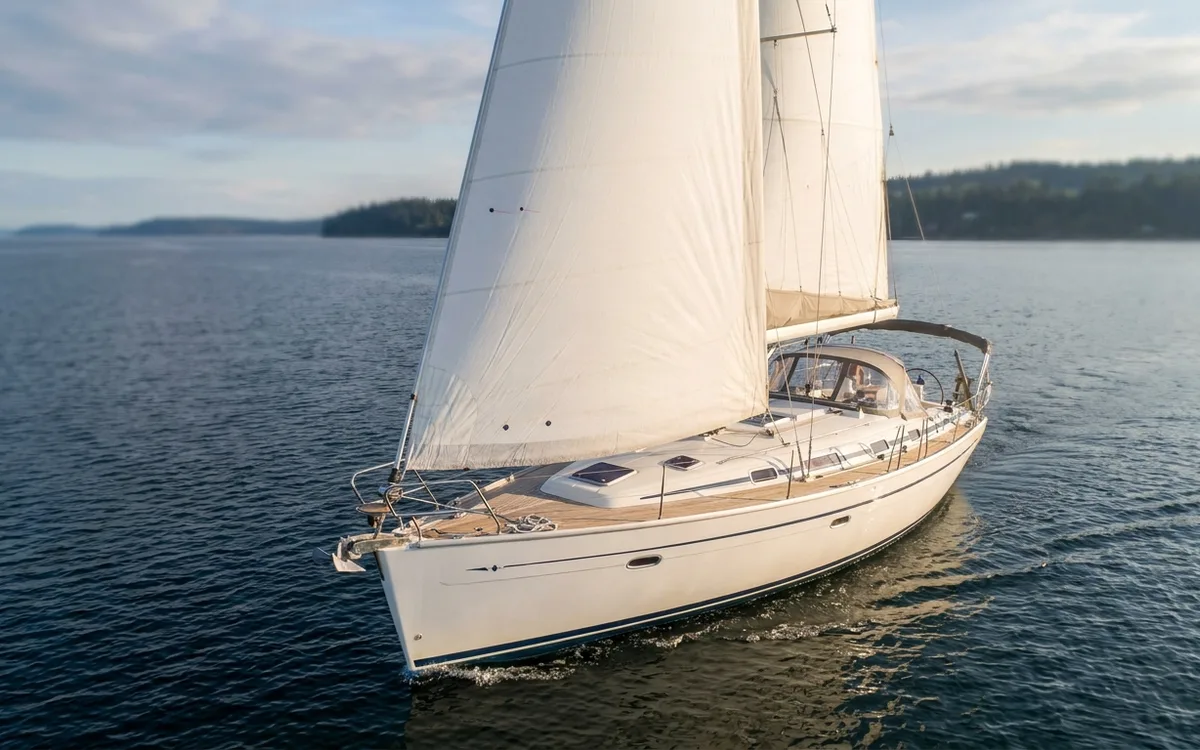 A well-kept Bavaria cruising yacht sailing along a quiet coast in late-afternoon light.