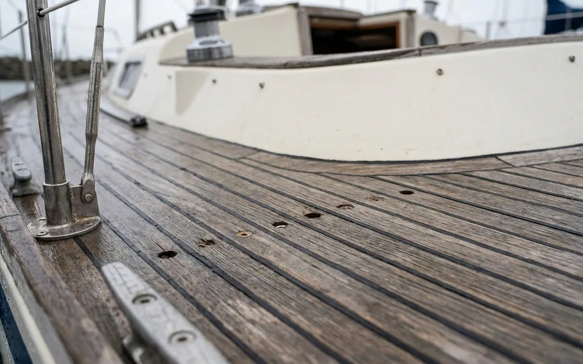 Worn teak side deck with proud caulking and missing screw-hole plugs on a used sailboat.