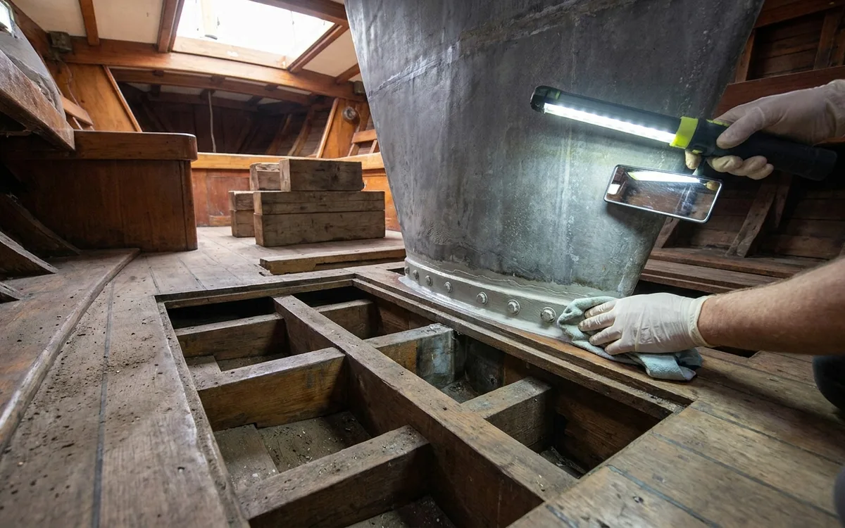 A surveyor checks the keel joint and internal floors for cracks or separation using a light and mirror.