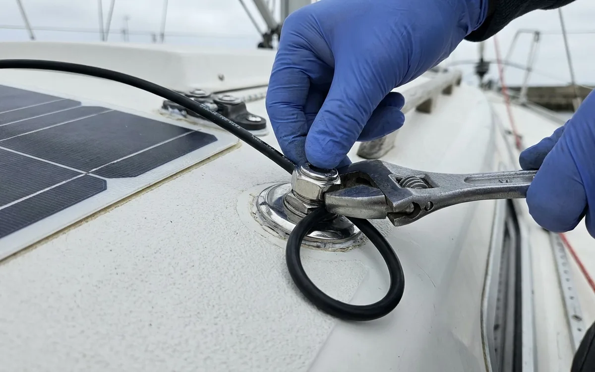 Hands tighten a sealed deck gland around a flexible panel cable on an HR29 coachroof.