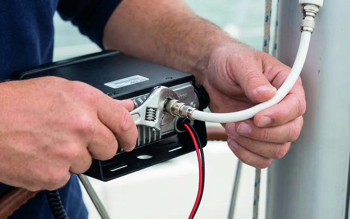 Hands tighten the VHF coax connector with the radio power disconnected, checking the aerial connection.