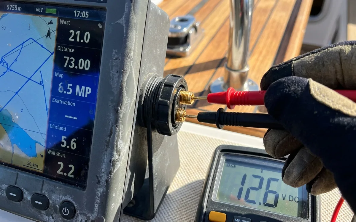 Hands measure voltage across a running chartplotter’s positive and negative power supply with a multimeter.