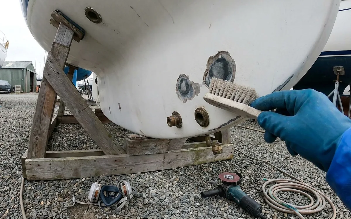 Freshly ground blister craters on a sailboat hull being scrubbed clean before epoxy repair.