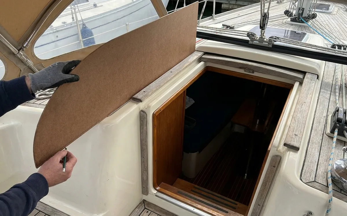 Hands mark a lower, slimmer hardboard dodger outline while checking clearance with the hatch open.