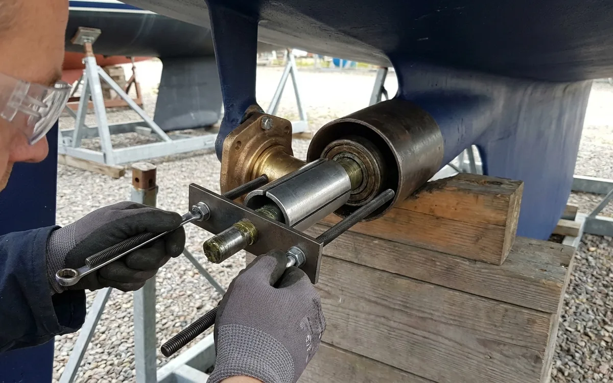 Hands tighten a bearing puller evenly to press a cutless bearing from a Malö 36 P-bracket.