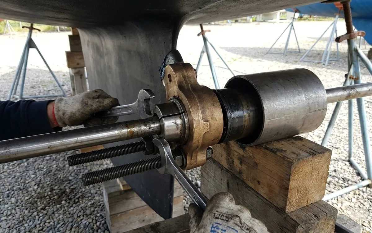 Hands tighten an M10 press to push the cutless bearing backward out of the bronze P-bracket over the shaft.