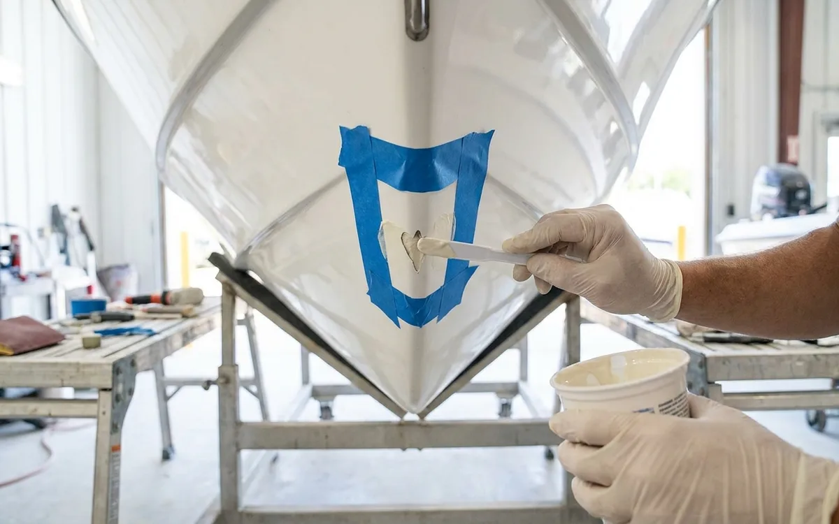 Fresh gelcoat being spread into a bevelled chip in a white fiberglass hull.