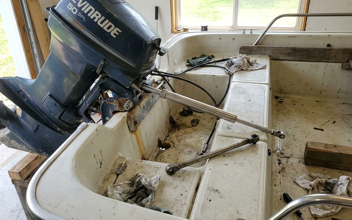 Steering cable ram partly withdrawn from an Evinrude tilt tube in a narrow Whaler splashwell.