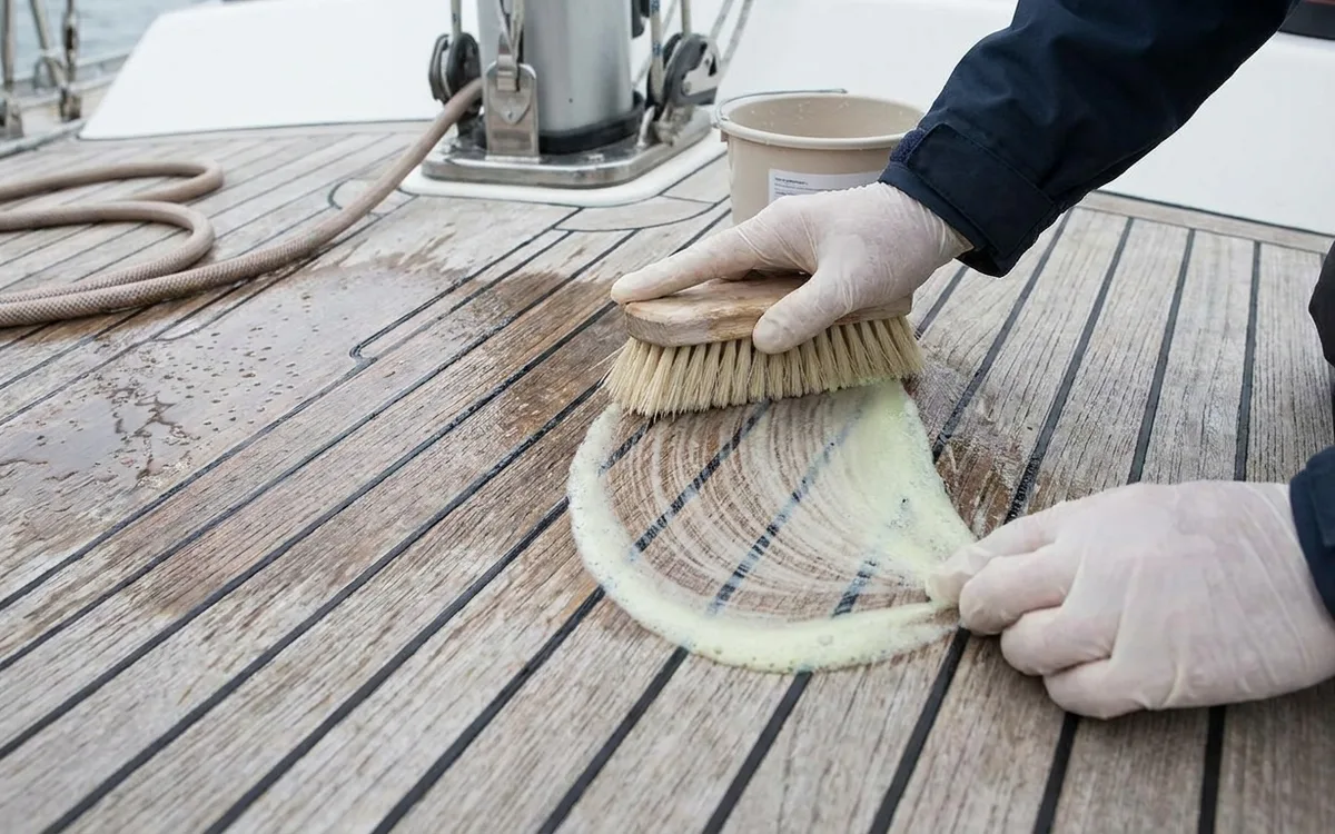 Hands gently brushing a teak deck across the grain with a soft brush and mild cleaner.
