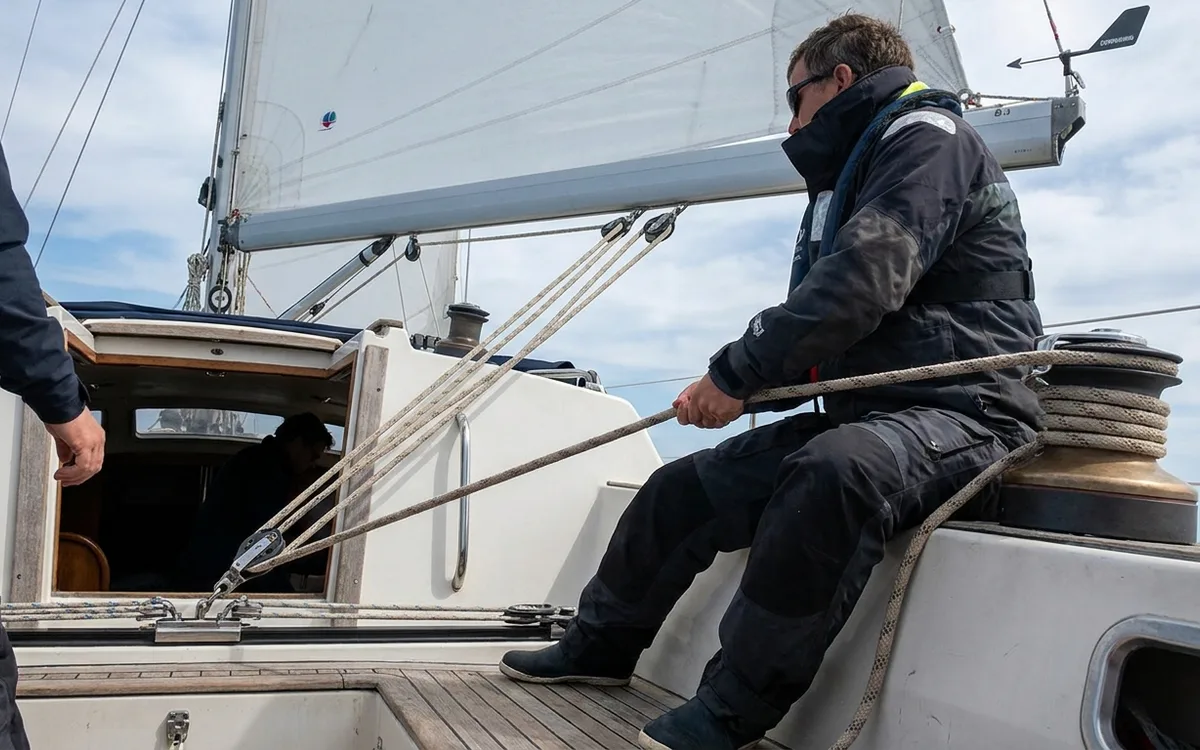 Crew member hauls the mainsheet to bring the boom toward the centerline before a controlled jibe.
