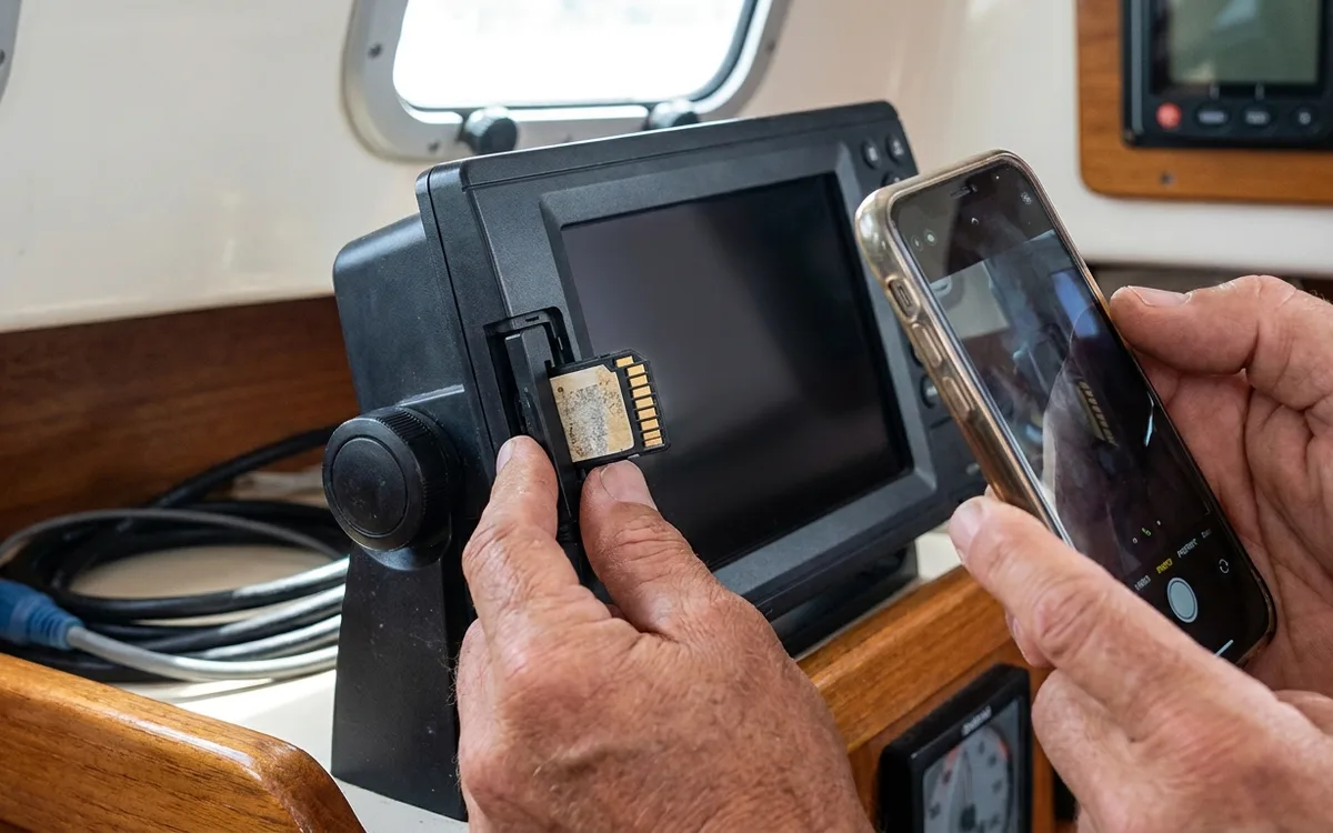 Hands remove a chart card from a powered-off chartplotter and photograph its label.