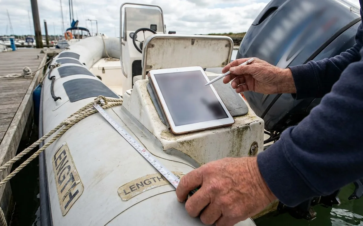 Hands verify a planing RIB’s length and outboard power before checking the licence requirement.
