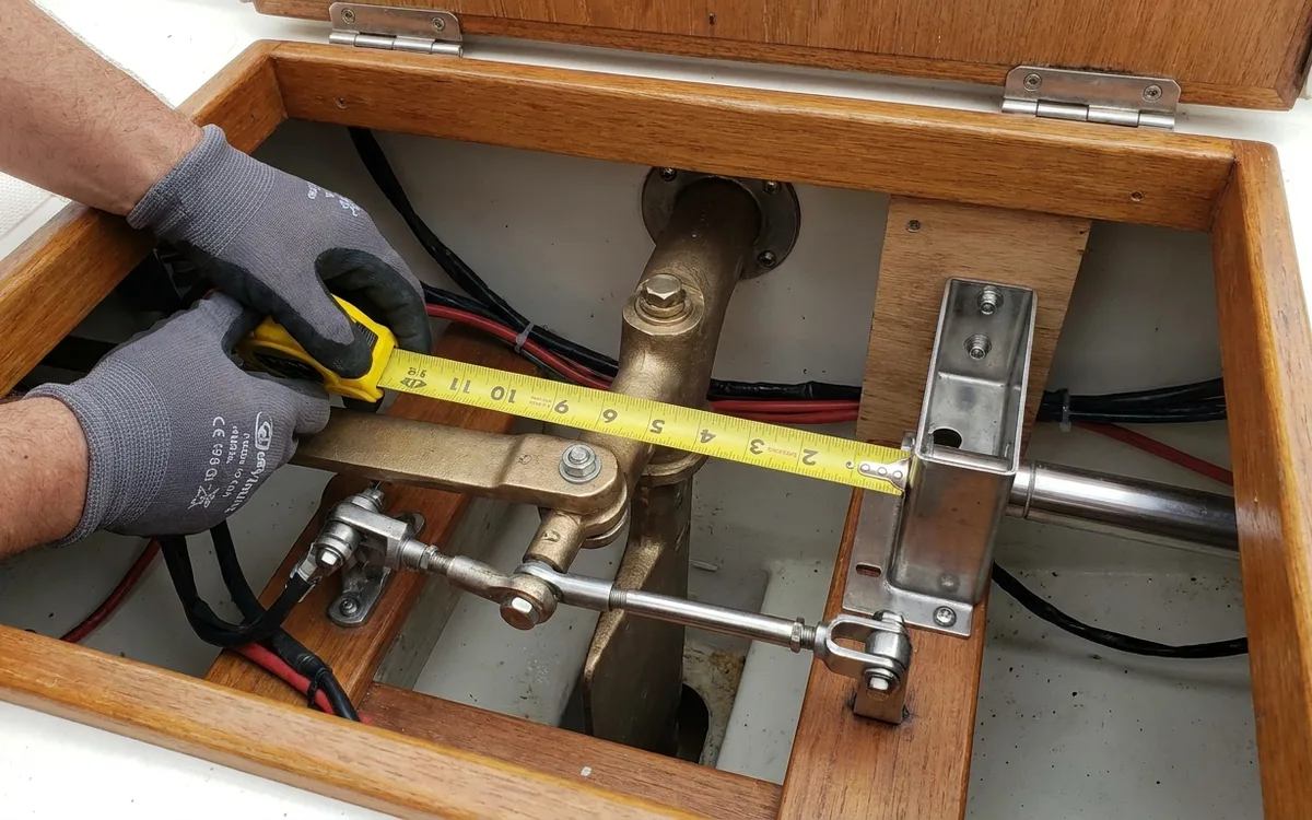 Hands measure rudder quadrant travel to check linear drive stroke and mounting geometry.