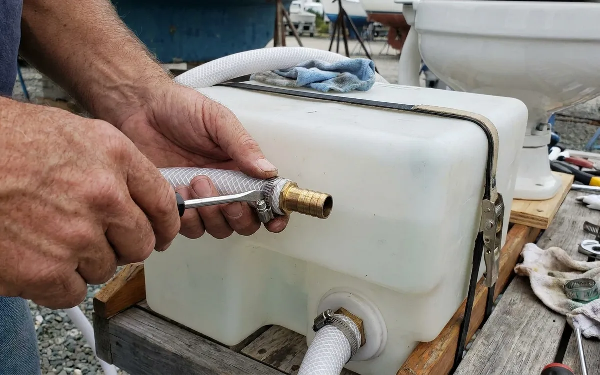 Hands tighten clamps on the sanitation hose joining a marine toilet discharge to the holding tank inlet.