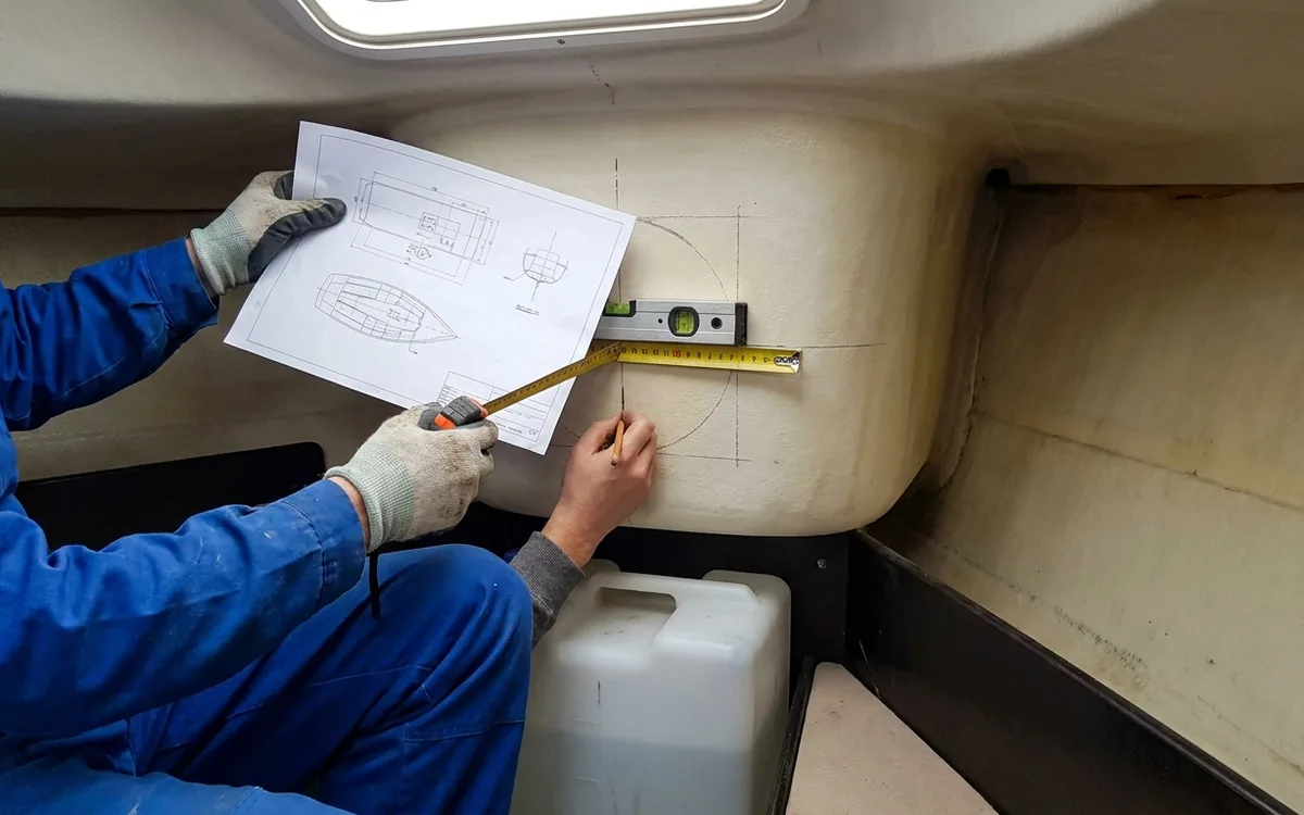 Technician checks tunnel position and clearance against a bow thruster installation drawing inside the forward berth.