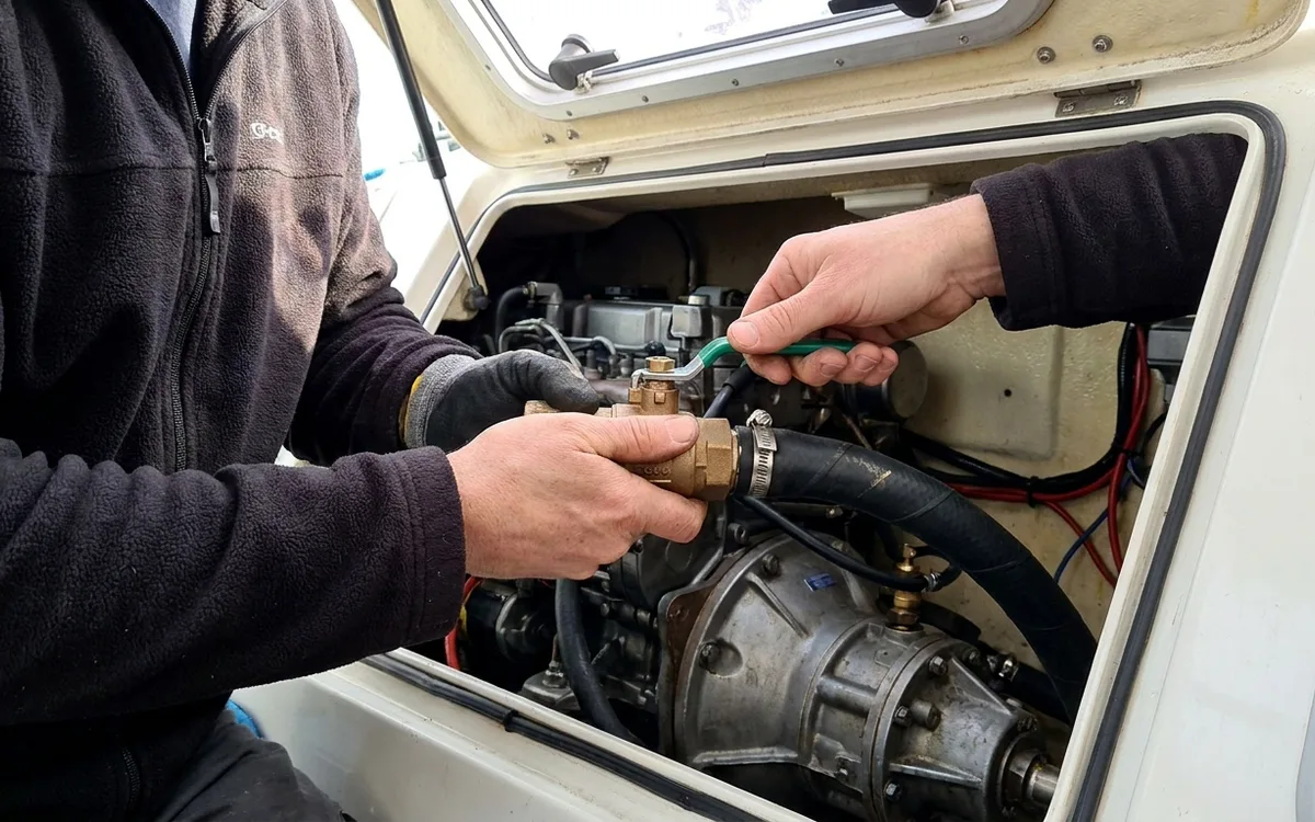 A sailor supports the saildrive seawater valve and gently checks its quarter-turn handle.