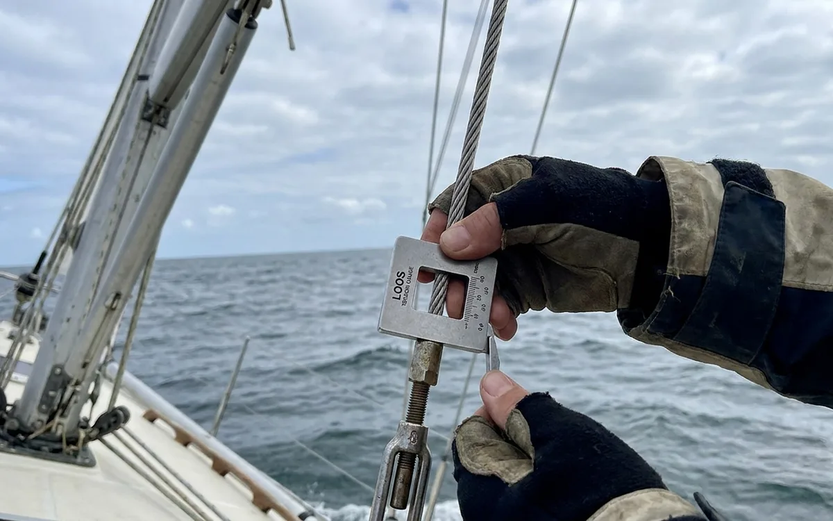 A sailor measures the leeward cap shroud with a tension gauge while the yacht is heeled.
