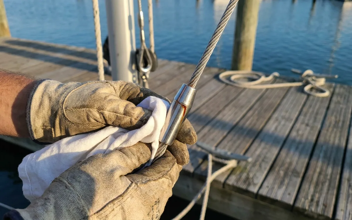 Gloved hands wipe and inspect a stainless shroud terminal at the wire entry for cracks or rust.