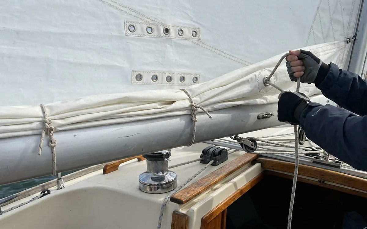Hands secure a reef in the mainsail, with the reef cringle hauled down snug to the boom.