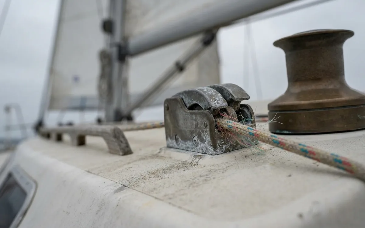 A fuzzy mainsail halyard passes through a worn rope clutch beside a sailboat winch.